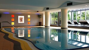 An indoor swimming pool with clear water, a tiled floor, and a view of the outdoors through large windows. - PHÖNIX Hotel (Bergneustadt)