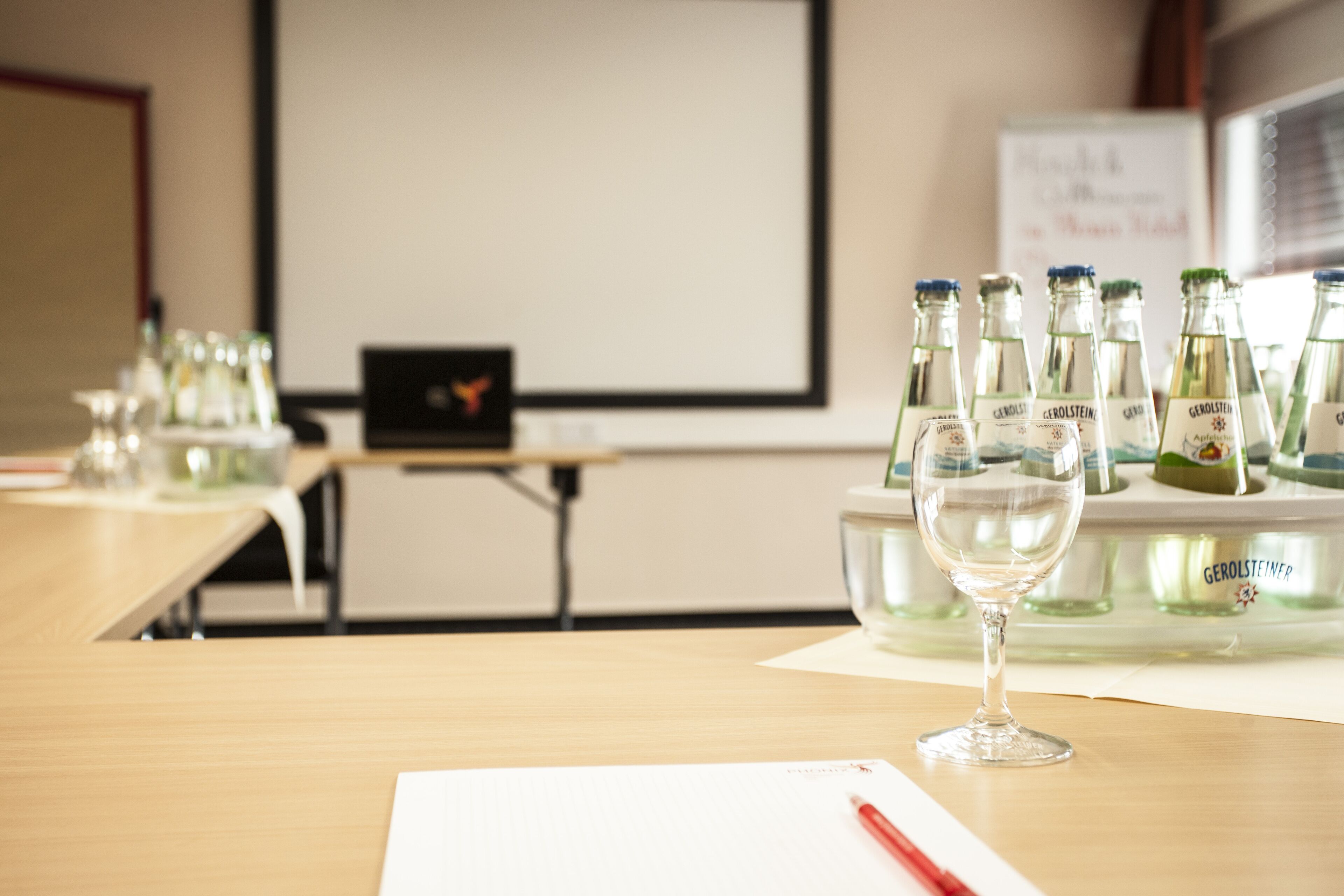 A conference room with a projector screen, tables with bottles of Gerolsteiner beer, and a glass on a table.