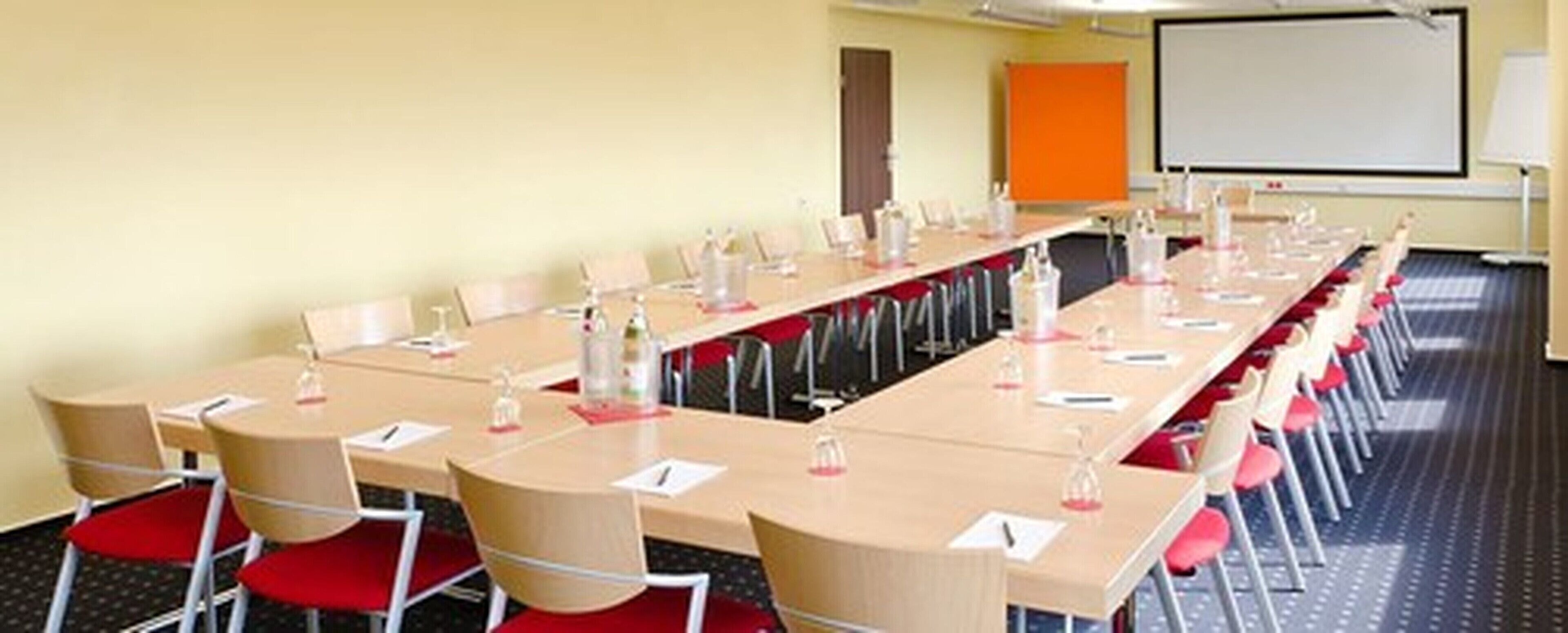 A conference room with multiple tables and chairs, equipped with water bottles and notepads.