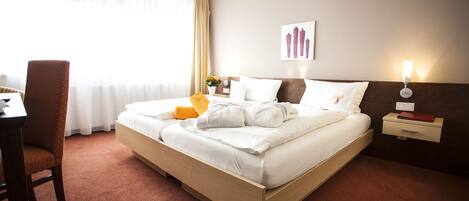 A hotel room with a bed, a chair, a nightstand, a lamp, and a window with curtains.