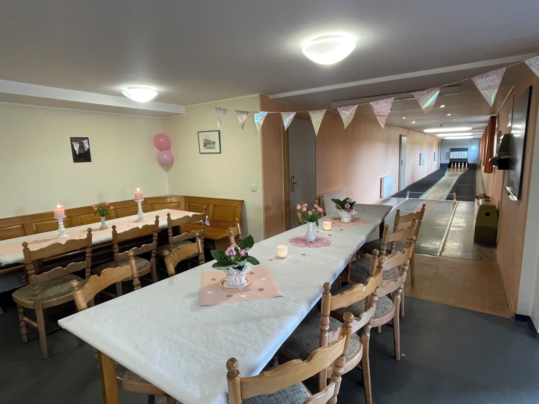 A dining area with long tables, wooden chairs, and a corridor leading to a room.