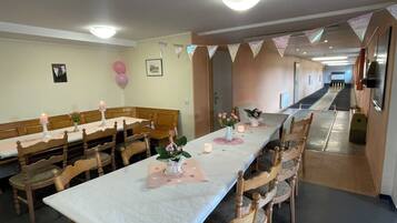 A dining area with long tables, wooden chairs, and a corridor leading to a room.