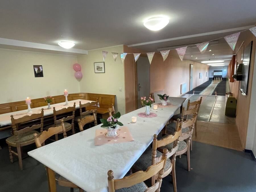 A dining area with long tables, wooden chairs, and a corridor leading to a room.