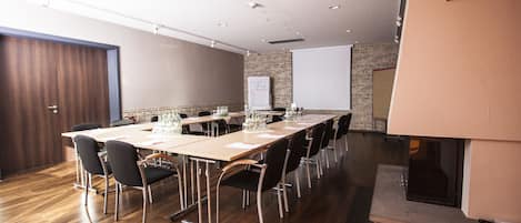 Un salón de conferencias con una larga mesa, sillas, una pantalla de proyector y una pizarra.