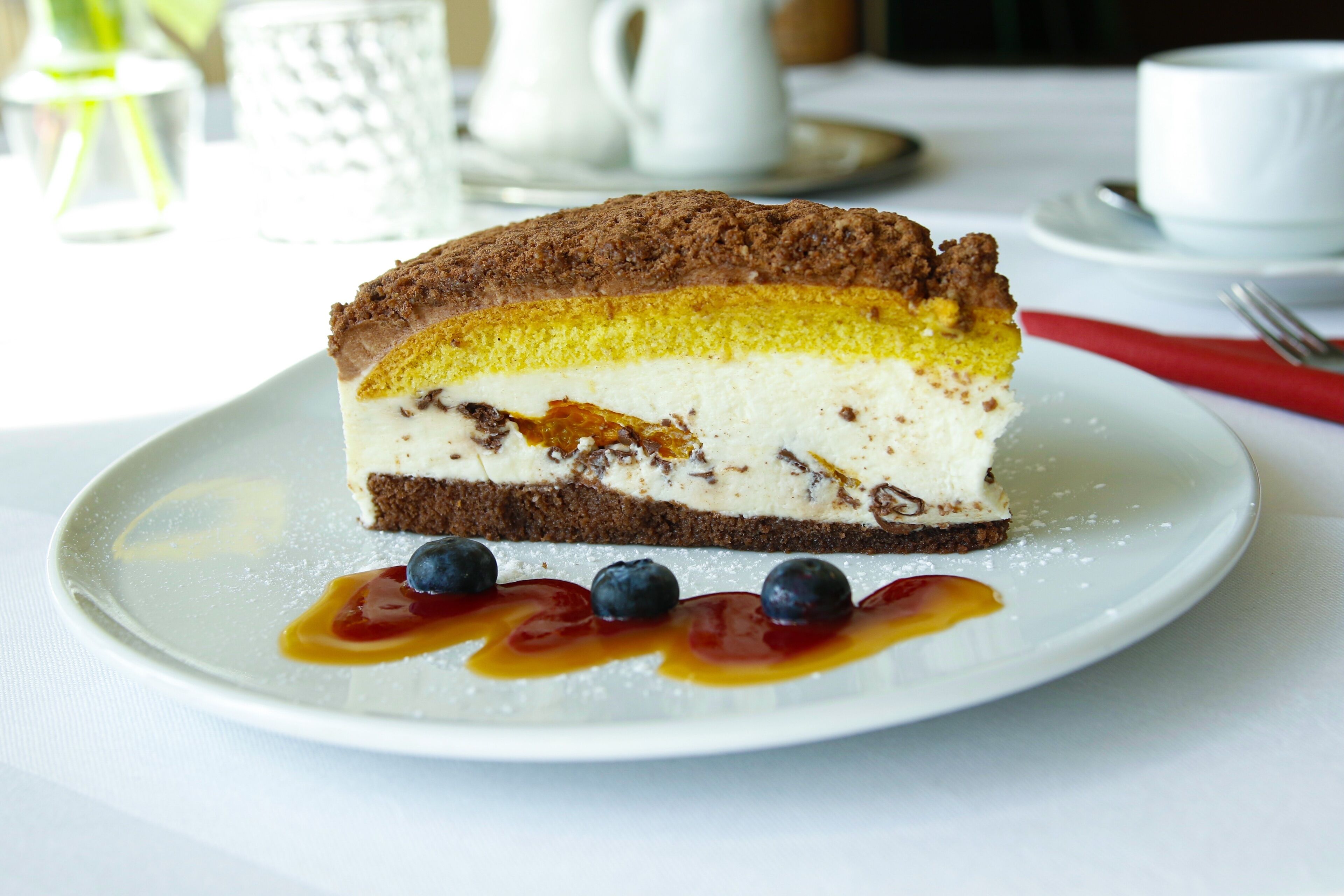 A slice of layered cake on a plate with blueberries and a sauce.