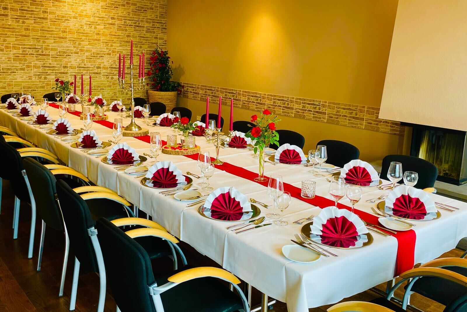 Una larga mesa de comedor decorada con vajilla roja y blanca, velas y un fondo de pared de ladrillo.
