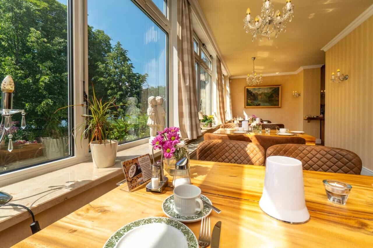 A dining area with a table set for two, a vase of flowers, and a view of the outdoors.
