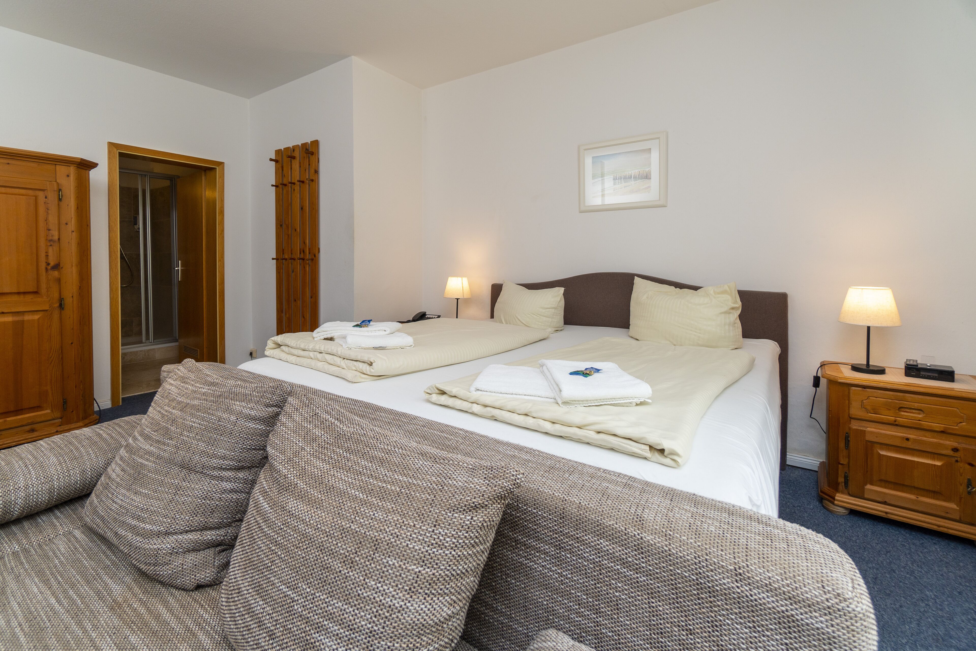 Une chambre d’hôtel avec un lit double, deux tables de chevet avec des lampes, une armoire en bois et une grande fenêtre.