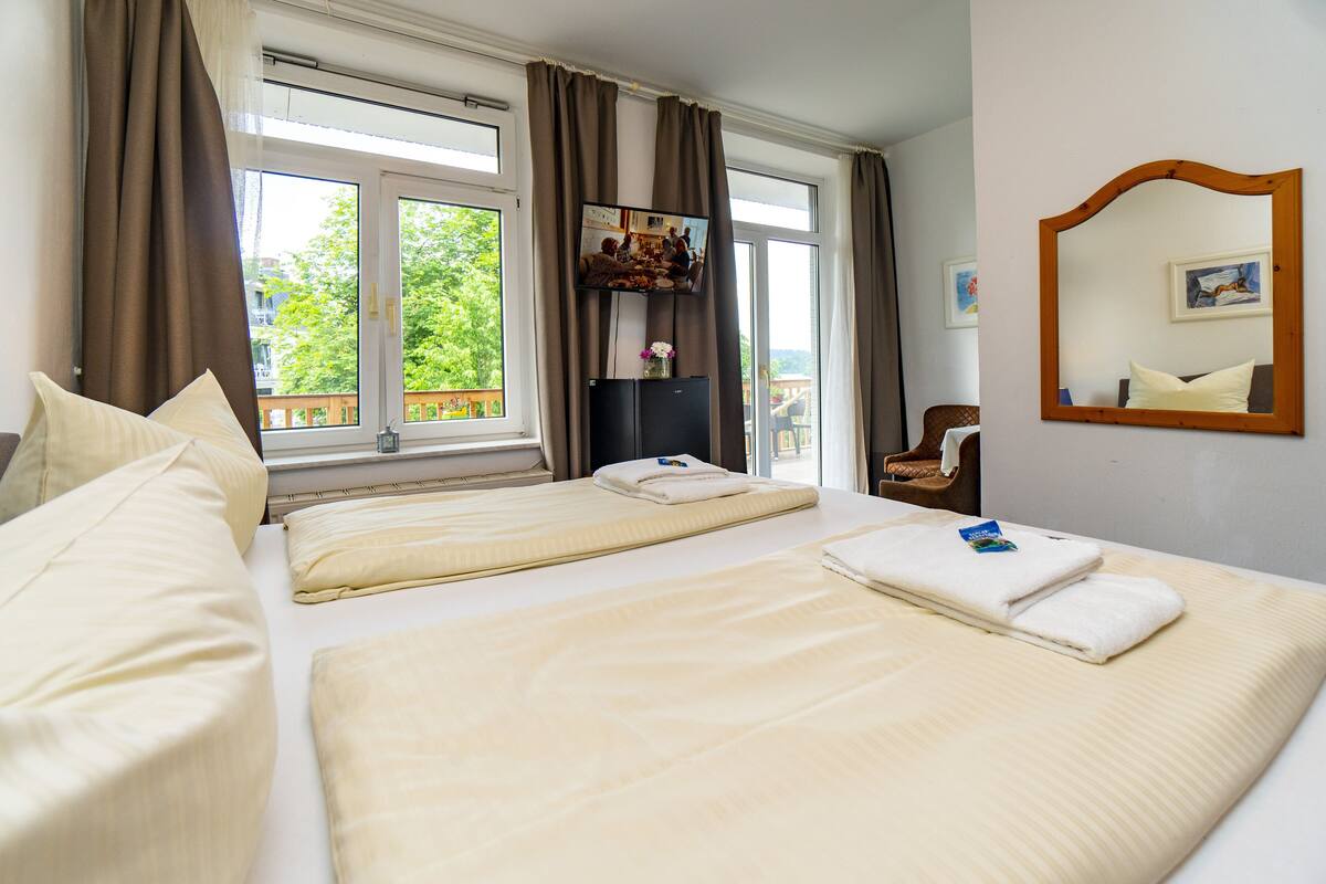 A hotel room with two beds, a TV, a window with curtains, a chair, and a mirror.