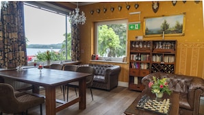 Una habitación acogedora con una mesa de madera, sillones de cuero, un tablero de ajedrez, una estantería y vistas al exterior.