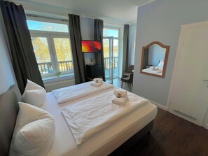 Habitación de hotel con una cama grande, televisión, espejo y balcón con vistas.