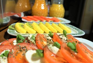 A table with plates of food, including sliced tomatoes and yellow fruit, and a glass of orange juice. - Hotel Holsteinische Schweiz (Malente)