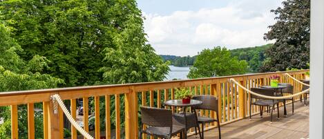 A wooden deck with wicker furniture and rope barriers, overlooking a river and dense greenery.