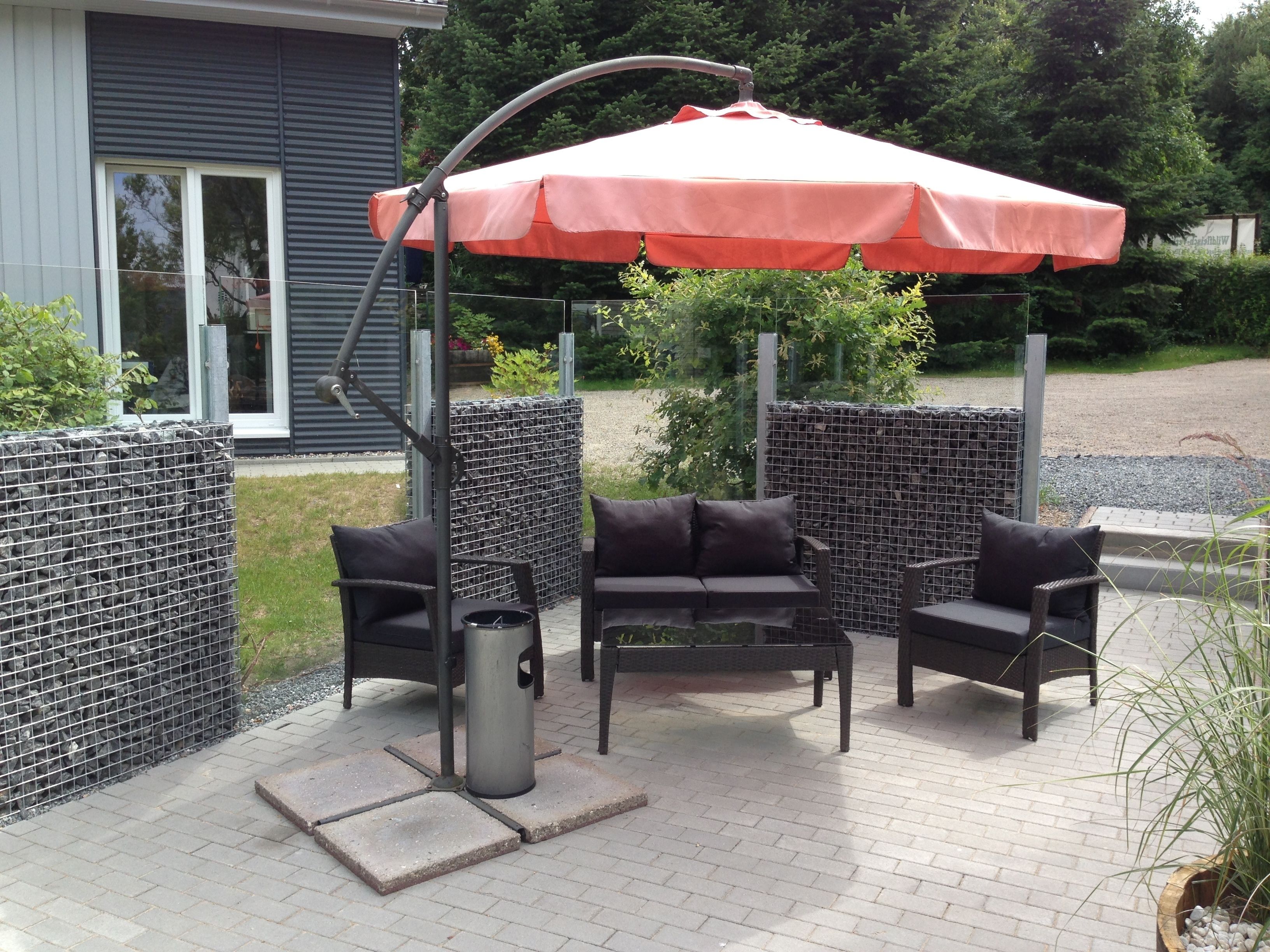 An outdoor patio with a metal grill, two black cushioned chairs, and a red umbrella.