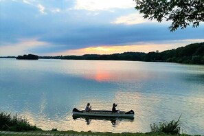 A calm lake with a small boat carrying two people, surrounded by greenery and a cloudy sky. - Hotel Holsteinische Schweiz (Malente)