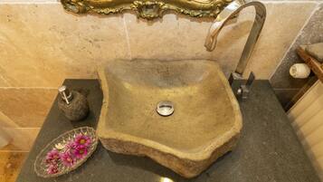 Un baño con un espejo grande y ornamentado, un lavamanos de piedra y un pequeño cuenco decorativo con flores.