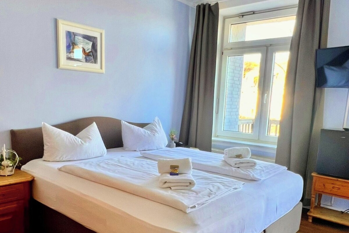 A hotel room with a large bed, a bedside table, a TV, and a window with curtains.