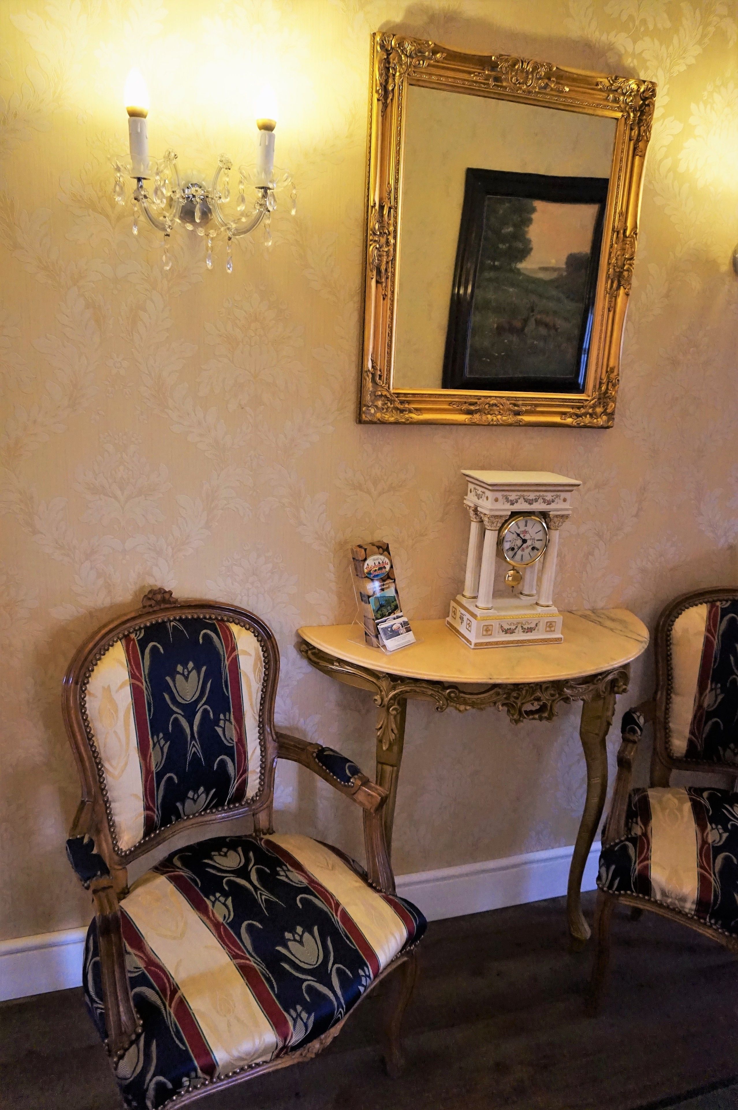 A vintage chair with a patterned upholstery, a wall-mounted clock, and a mirror with an ornate frame.