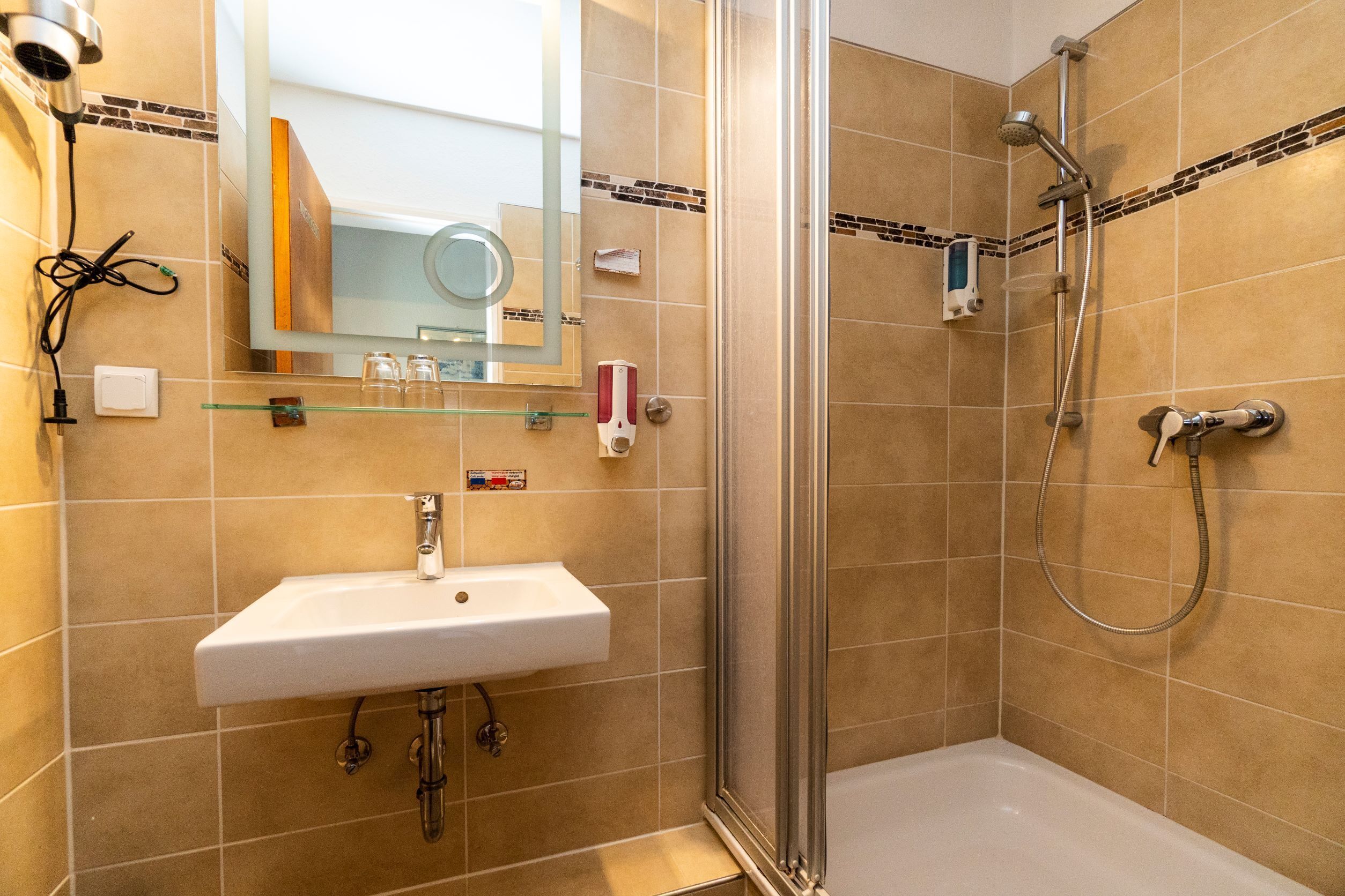A bathroom with a glass shower enclosure, a white sink, and a mirror above it.