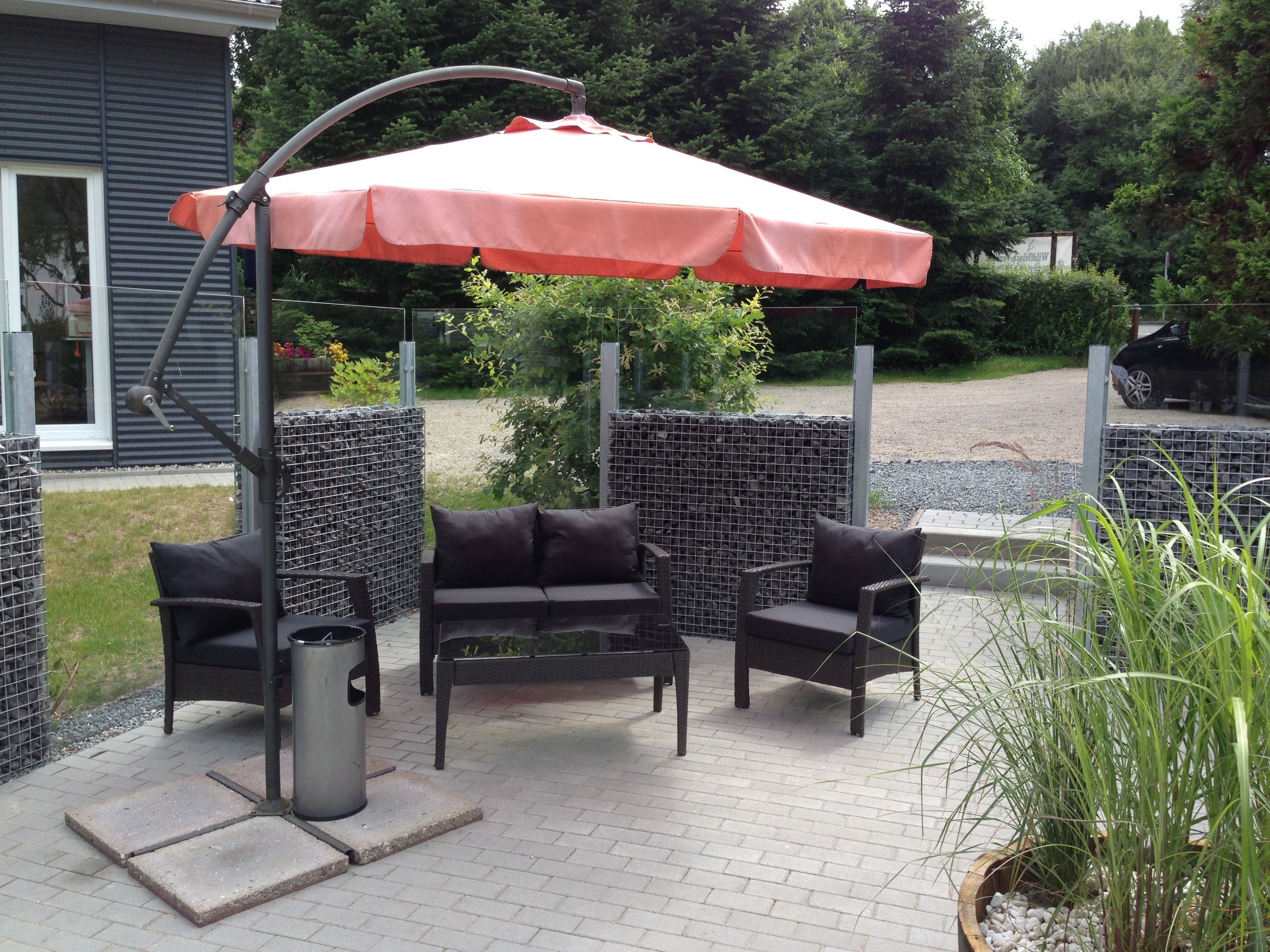 Un espace extérieur aménagé avec des sièges, notamment une chaise suspendue, et un parasol rouge.