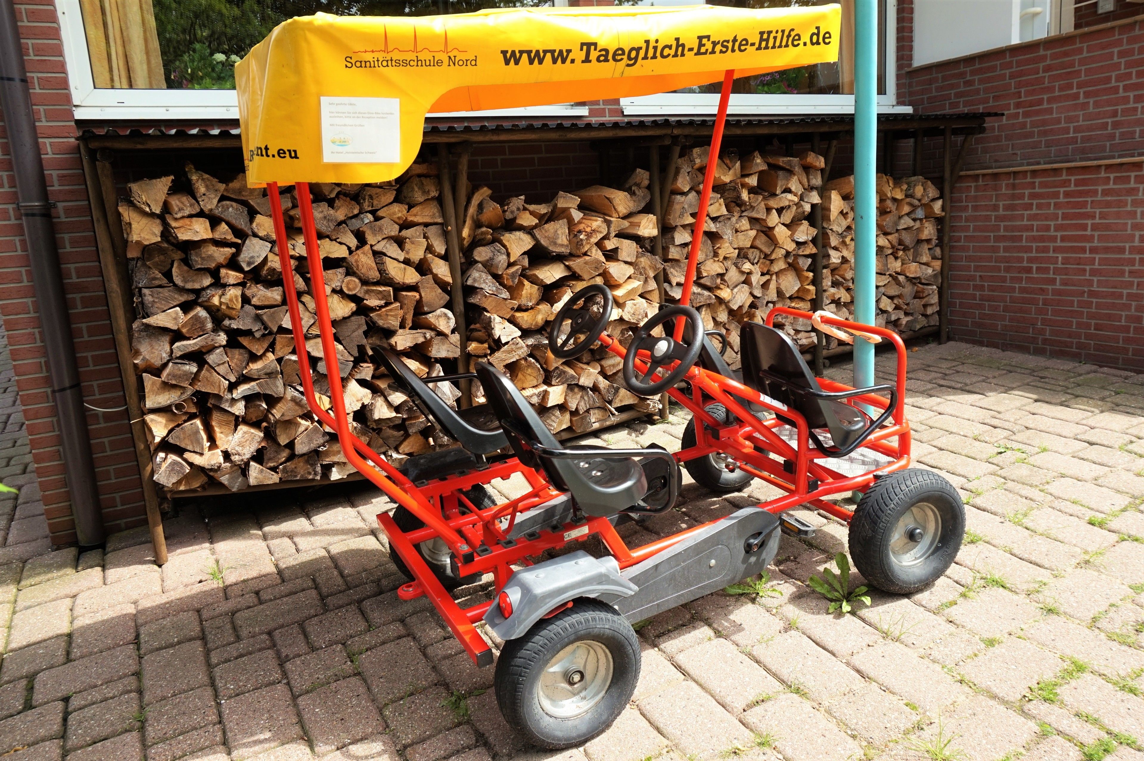 A red and gray lawnmower with a yellow canopy labeled "Sanitatschule Nord" and a website address.