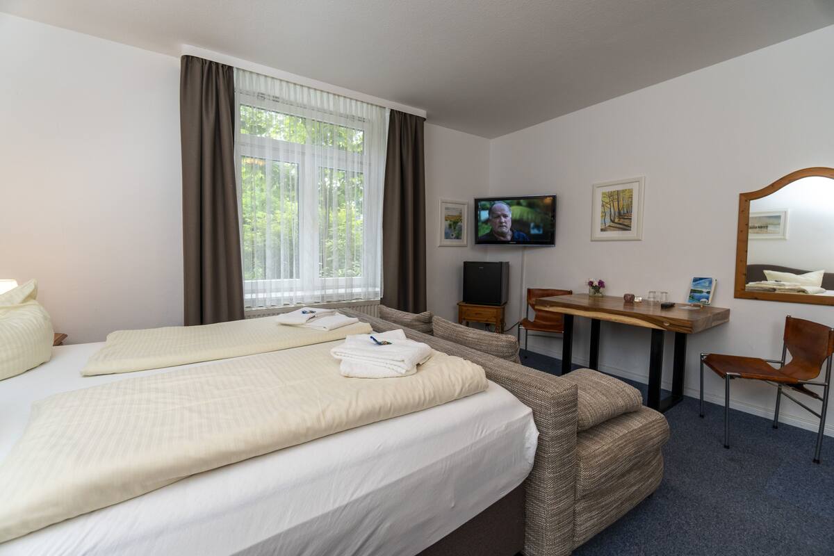 A hotel room with two beds, a TV, a desk, and a chair.