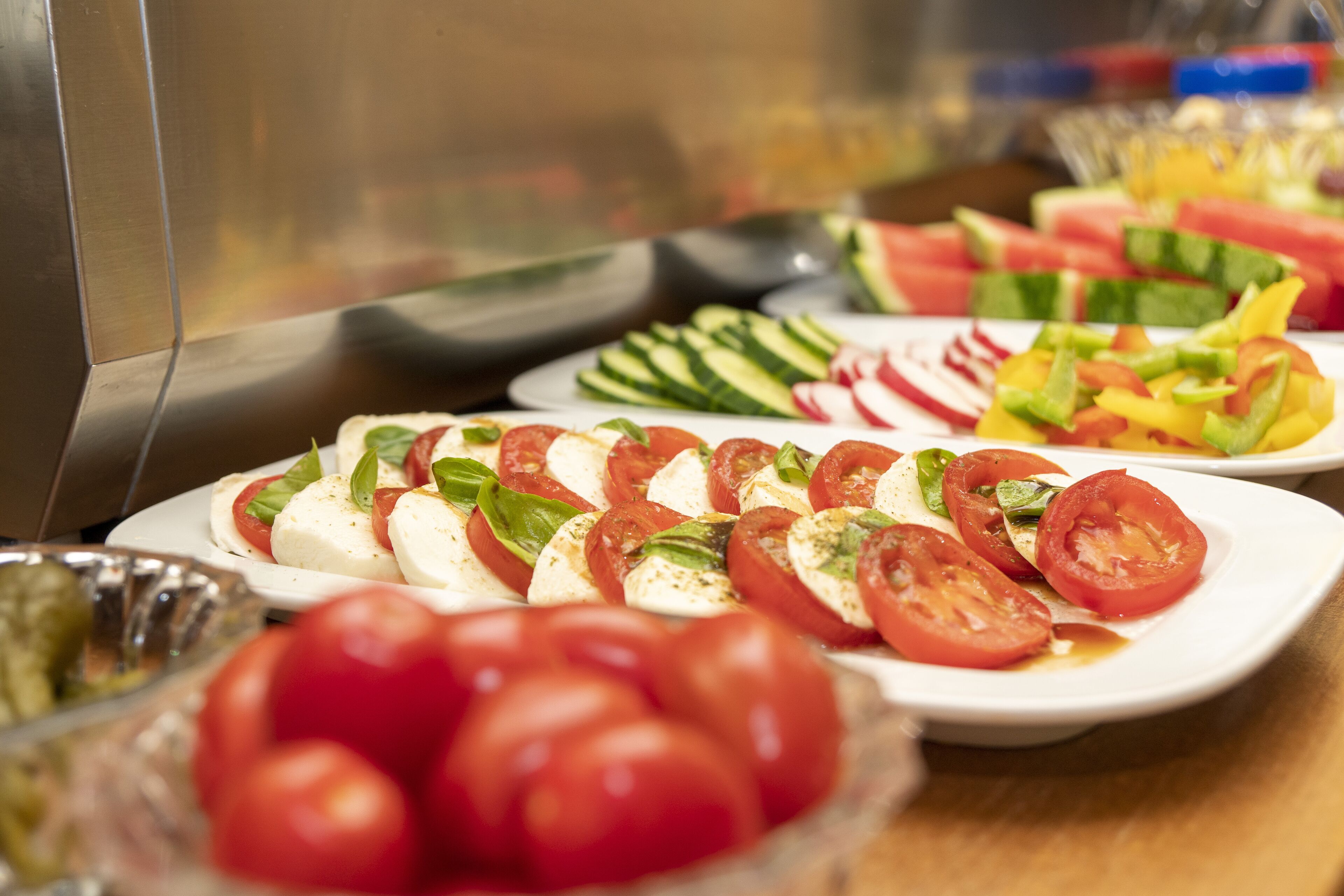 A buffet table with various dishes including sliced tomatoes, cucumbers, and watermelon.