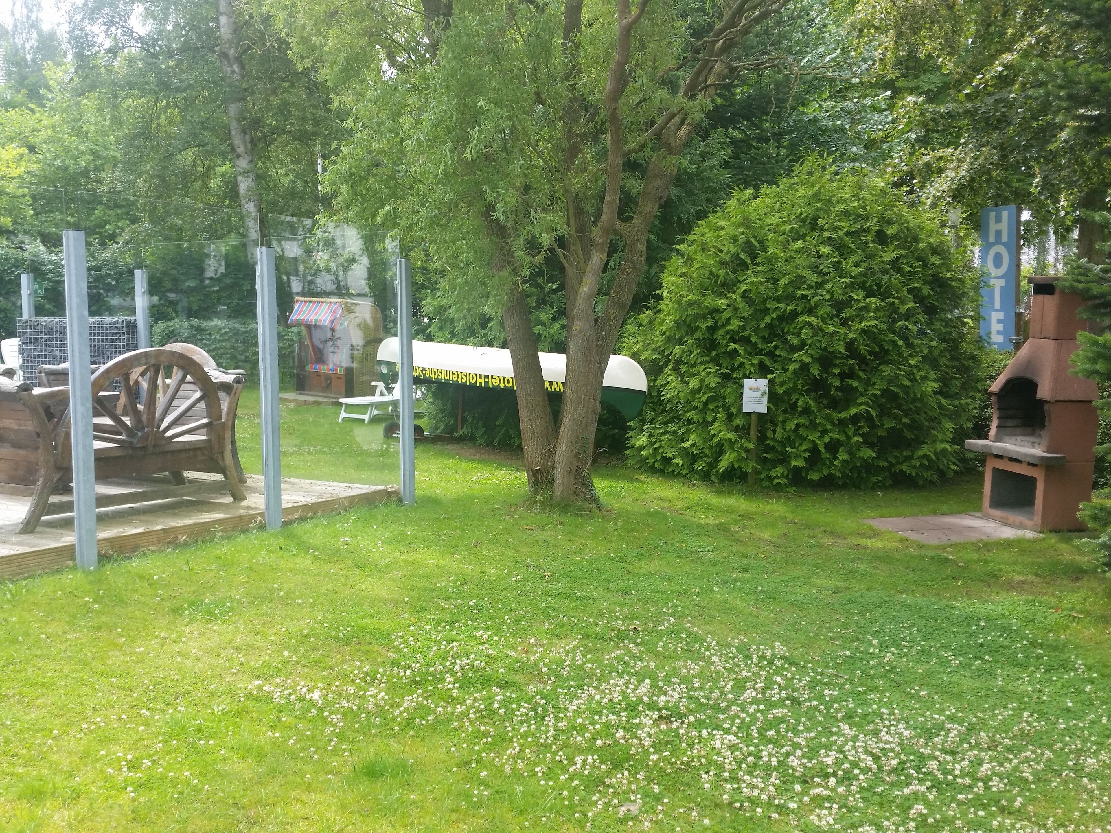 A grassy outdoor area with a wooden cart, a barbecue grill, and a covered seating area.