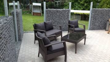 An outdoor patio area with wicker furniture and a glass table.