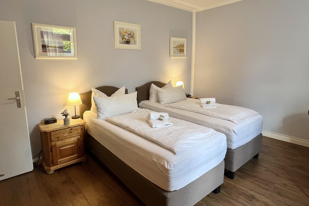 A hotel room with two beds, bedside tables with lamps, and framed pictures on the wall.