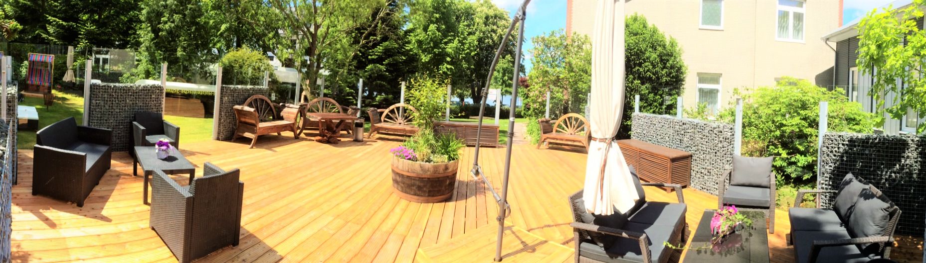 An outdoor patio area with wooden flooring, wicker furniture, and a central planter with flowers.