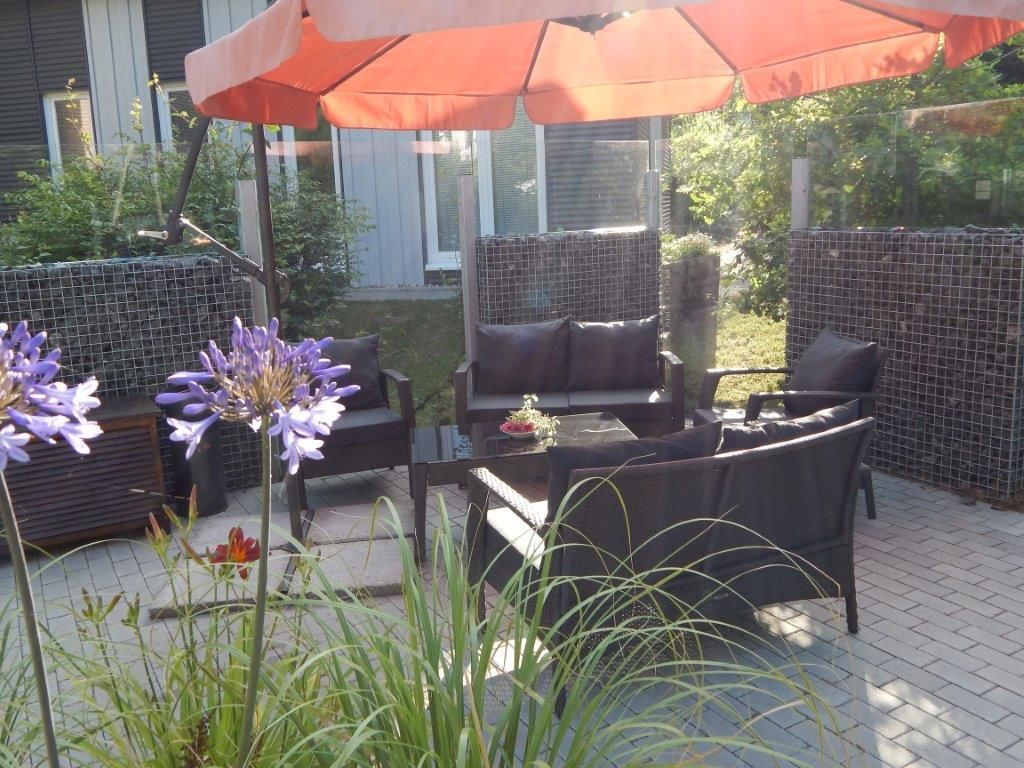 Eine Außenpatio mit Esstisch und Stühlen, umgeben von einer Ziegelmauer und beschattet durch einen großen Sonnenschirm.