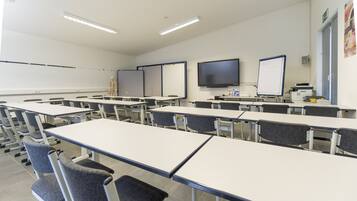 A classroom with rows of desks and chairs, a whiteboard, a projector, and a skeleton model on a table.