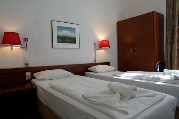 A hotel room with two beds, a wooden wardrobe, a framed picture on the wall, and two wall-mounted lamps. - Hotel Xantener Eck (Berlin)