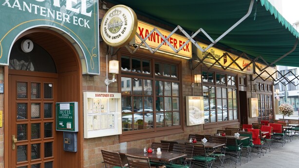 A hotel exterior with a green awning, outdoor seating area, and a sign indicating the hotel name. - Hotel Xantener Eck (Berlin)