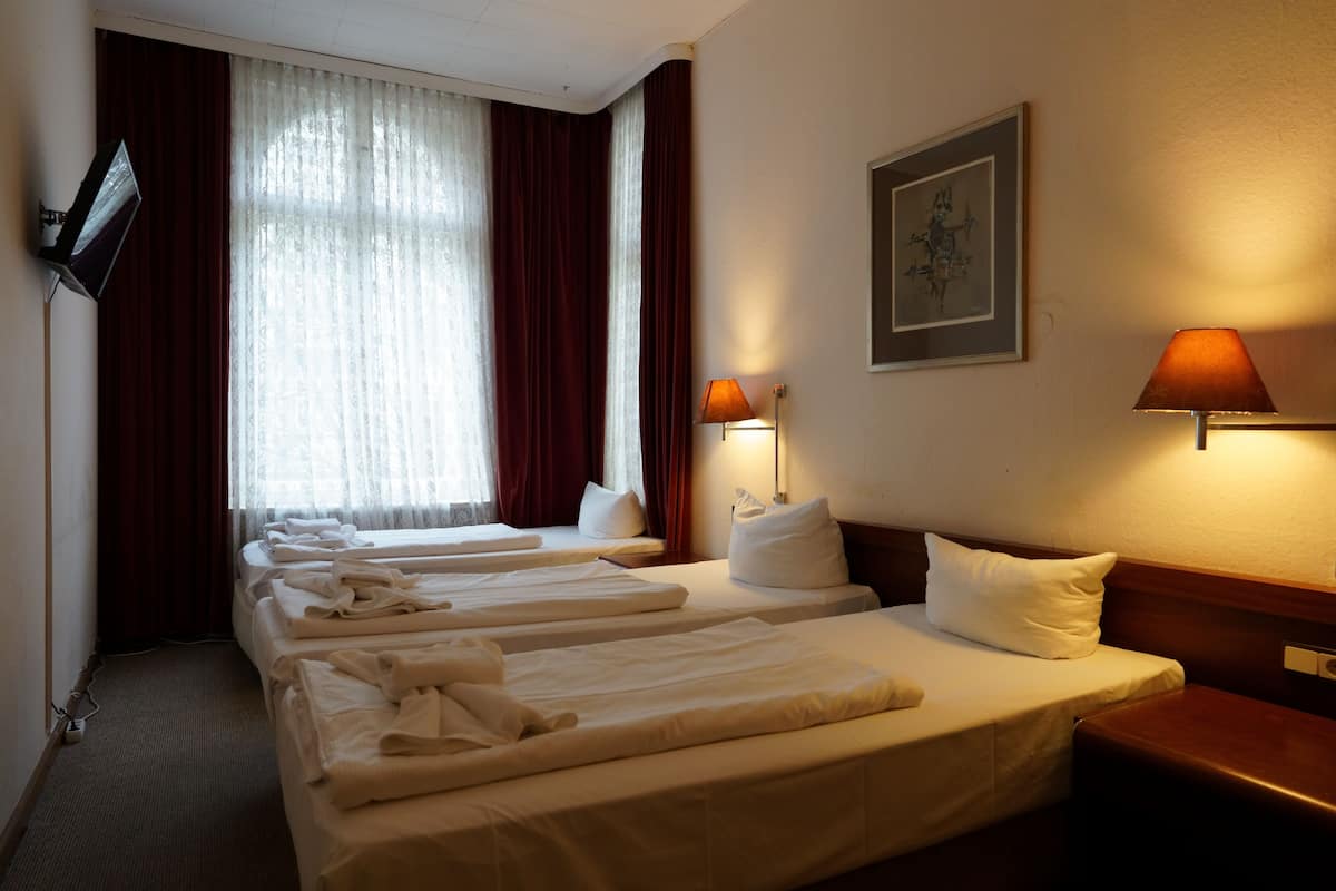 A hotel room with four single beds, a TV mounted on the wall, a painting, and two bedside lamps.