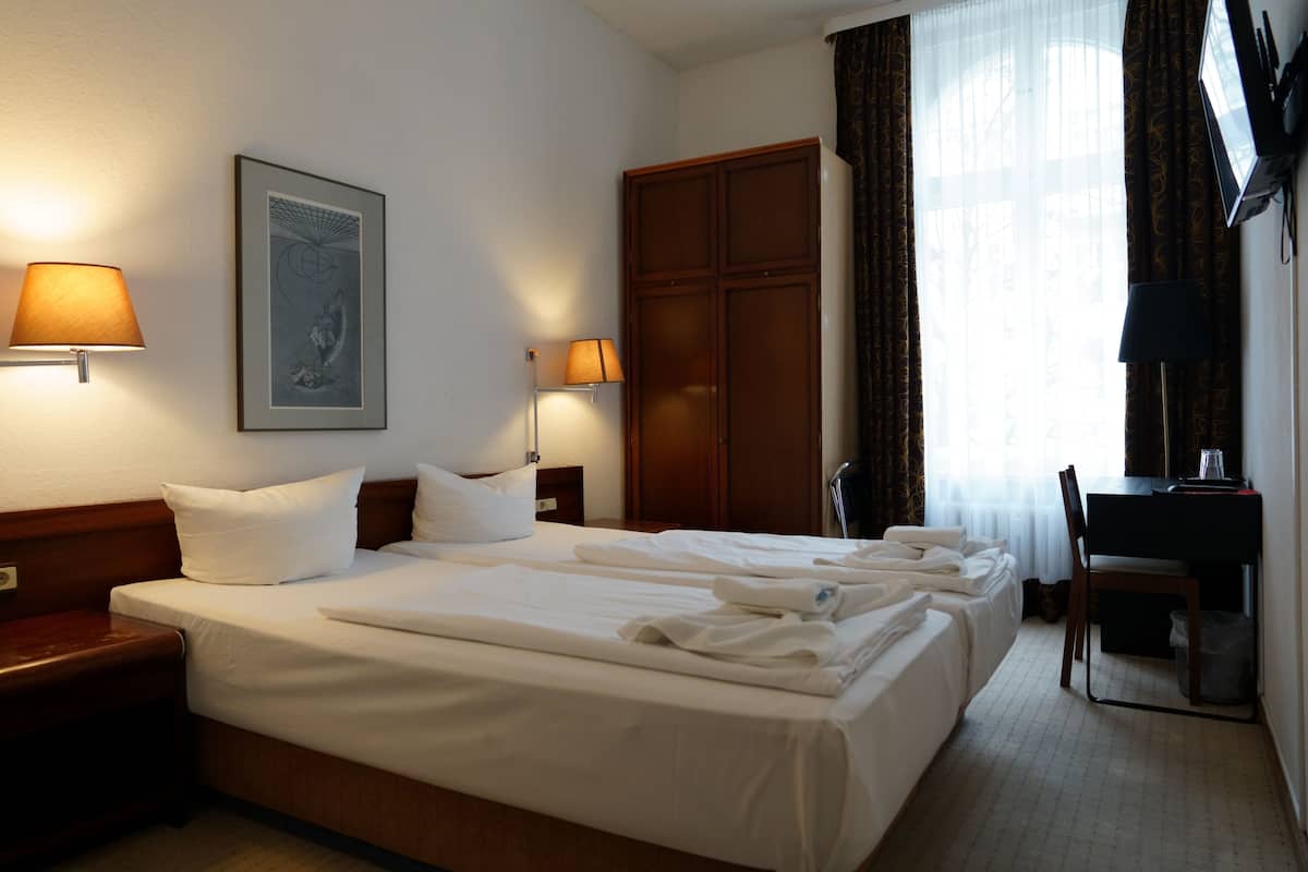 A hotel room with a large bed, two bedside lamps, a desk, and a wardrobe.