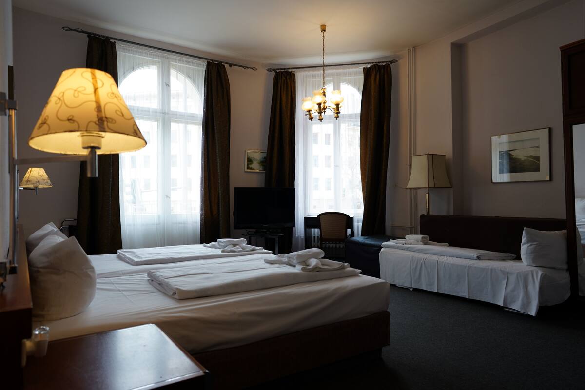 A hotel room with two beds, a desk, a chair, a television, and a chandelier.