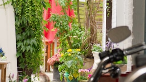 A motorcycle parked in a garden with potted plants and a red umbrella in the background. - Hotel Cafe Frida (Bredstedt)