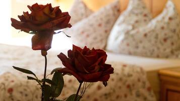Un lit avec une literie à motifs floraux et des oreillers, un vase contenant deux roses et une table de chevet en bois.