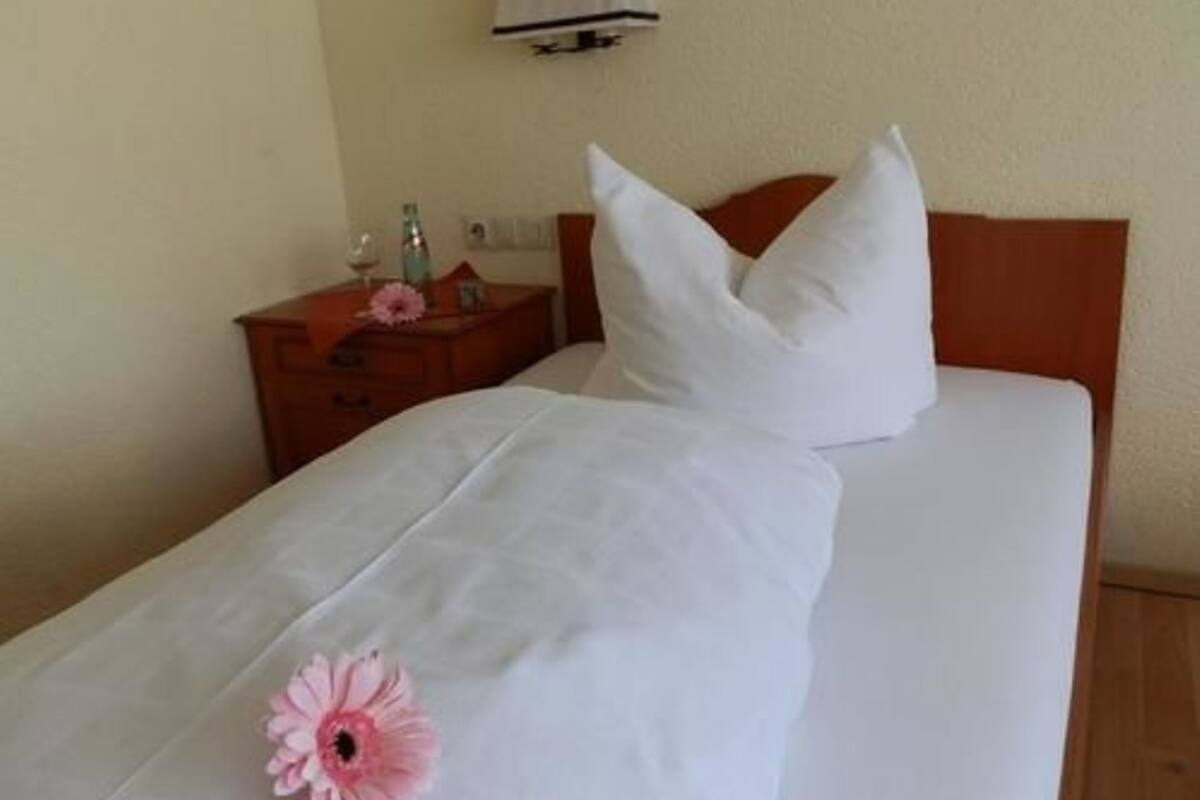 A hotel room with a bed, a nightstand, a lamp, and a wall-mounted air conditioning unit.