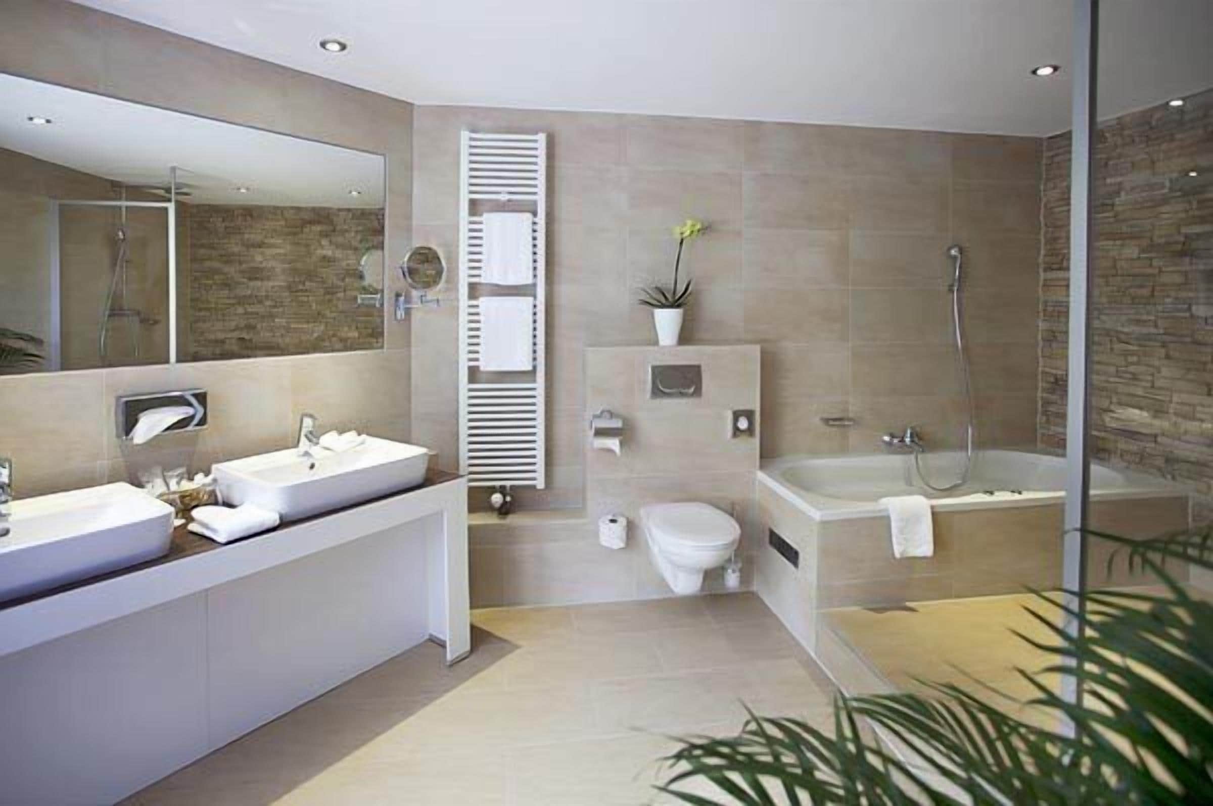 Ein modernes Badezimmer mit einem großen Spiegel, zwei Waschbecken, einer Toilette, einer Badewanne und einer Dusche.