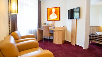 Quarto de hotel com escrivaninha, uma cadeira, cama, televisão e um retrato grande na parede.