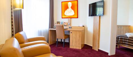 Habitación de hotel con escritorio, una silla, una cama, televisión y un cuadro grande en la pared.