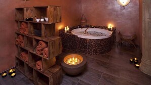 Un área de spa con una bañera de hidromasaje circular, estantes de madera con toallas y una chimenea central.