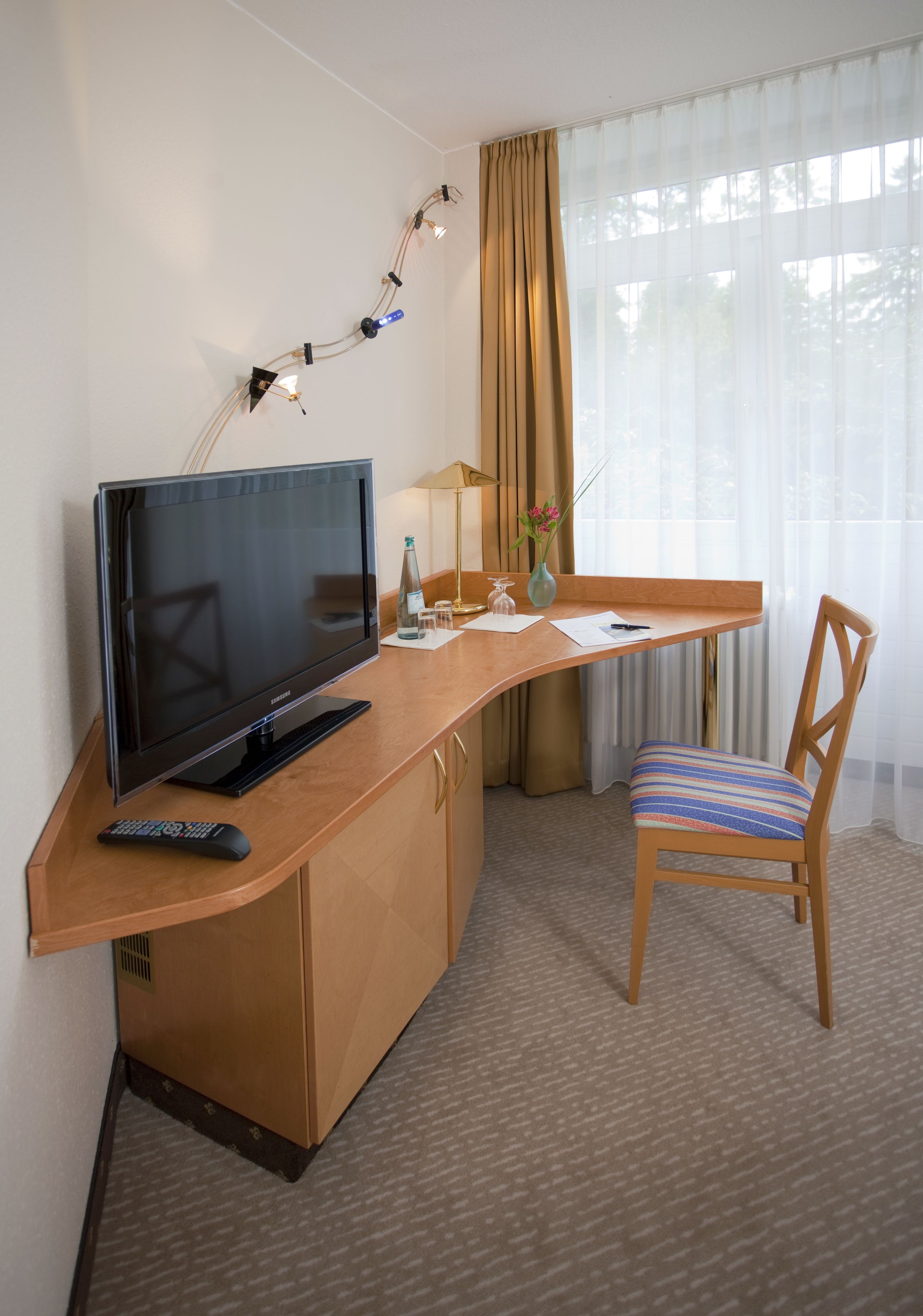 Ein Hotelzimmer mit einem Holztisch, einem Fernseher, einer Fernbedienung, einer Vase mit Blumen und einem Sessel.