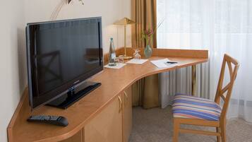 Ein Hotelzimmer mit einem Holztisch, einem Fernseher, einer Fernbedienung, einer Vase mit Blumen und einem Sessel.