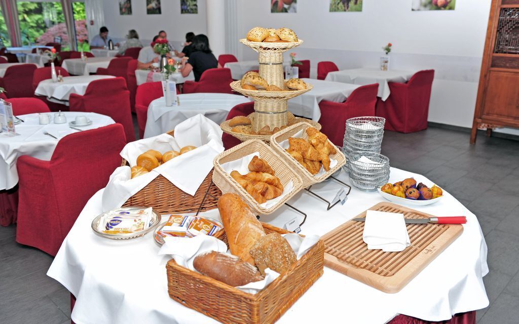 Ein reichhaltiges Buffet mit verschiedenen Brotsorten und Gebäck auf Tischen, umgeben von roten Stühlen und weißen Tischdecken in einem Essbereich.