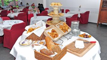 Ein reichhaltiges Buffet mit verschiedenen Brotsorten und Gebäck auf Tischen, umgeben von roten Stühlen und weißen Tischdecken in einem Essbereich.
