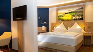 Un dormitorio moderno con una cama grande, un televisor montado y un cuadro de un paisaje pintoresco sobre la cama.